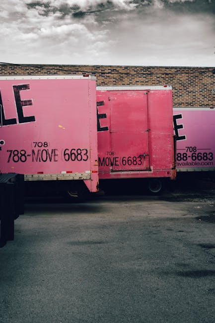 A collection of cardboard boxes of various sizes, some labeled with 'FRAGILE HANDLE WITH CARE' stickers, are loaded into the back of a van, ready for a home relocation. The boxes are stacked neatly on